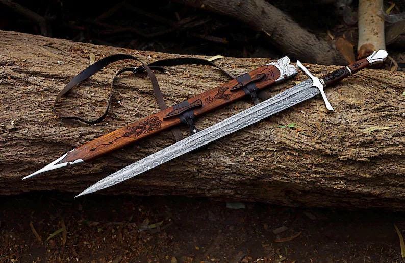 May include: A double-edged sword with a patterned Damascus steel blade, a silver crossguard, and a dark wooden handle with a silver pommel. It is accompanied by a matching wooden scabbard featuring intricate carvings and a black leather strap.