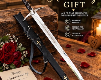 May include: A silver-toned metal sword with a dark handle and a circular pommel detail, accompanied by a black leather scabbard featuring gold-colored cross emblems. The sword blade is engraved with text, and the set is displayed with red roses.