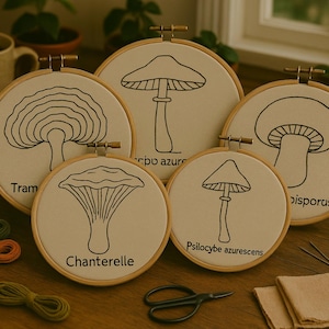 Pode incluir: Cinco aros de bordado com diferentes desenhos de cogumelos. Os aros estão sobre uma mesa de madeira com fio de bordar e agulhas. Os desenhos incluem "Tram", "Cripo Azure", "Chanterelle", "Psilocybe azurescens" e "Bisporus".