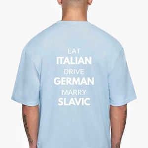Puede incluir: Camiseta azul claro con la frase blanca: "EAT ITALIAN DRIVE GERMAN MARRY SLAVIC". La camiseta tiene mangas cortas y cuello redondo.