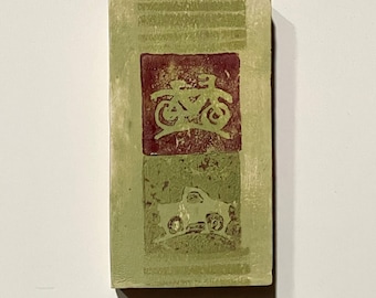 May include: A rectangular, light green block with a textured surface. It features two red squares, each with a light green image. The top square has a bicycle image, and the bottom square has a car image.
