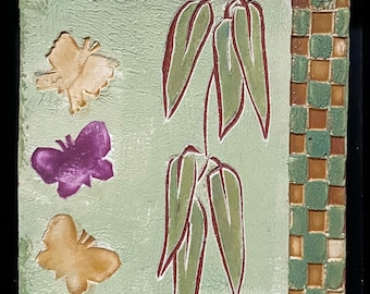 May include: Square, textured artwork with a light green background. Features three embossed butterflies in shades of gold and purple. A stylized plant with green leaves and red outlines is in the center. A vertical border of small, square tiles in green and brown.