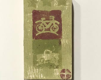 May include: Rectangular, textured, green and white block with a bicycle and truck design. The block has a red square with a bicycle image, a green square with a truck image, and three green stars at the top.