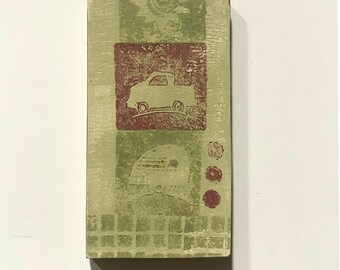May include: A rectangular, hand-painted wooden block with a green and burgundy design. The block features a truck, sun, and other geometric shapes. The color palette includes shades of green, burgundy, and white.