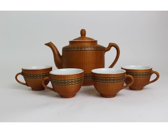 May include: A tea set consisting of one teapot with a lid and four matching teacups. Each piece is made of brown ceramic with a textured vertical ribbed surface and a horizontal band featuring a dark brown and black geometric pattern.