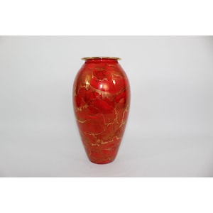 May include: A decorative vase with a glossy red finish and gold veining. The vase has a rounded body and a slightly flared rim with a gold band. The shape is similar to a classic urn.
