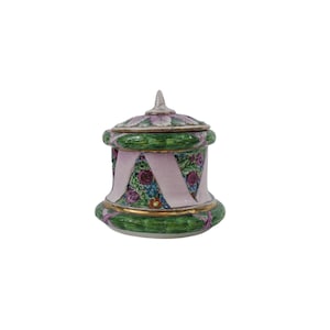 Könnte beinhalten: Ein dekoratives Keramikgefäß mit Deckel. Das Gefäß ist zylindrisch mit ausgestelltem Boden und weist ein Blumendesign mit rosa Bändern und grünen Akzenten auf. Der Deckel ist mit einer spitzen Spitze verziert.