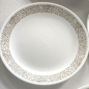 Puede incluir: Un plato de cena de cerámica blanca con un diseño floral marrón alrededor del borde.