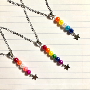 May include: Three silver chain necklaces with rainbow-colored bead strands and a star charm. The beads are arranged in a gradient of colors, from red to purple. The star charms are silver.