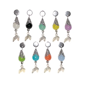 Peut inclure: Collection de neuf boucles d'oreilles pendantes avec des perles en forme de goutte d'eau de différentes couleurs. Chaque boucle d'oreille comporte un capuchon en filigrane argenté, une petite perle transparente et un charm en forme de feuille argentée.