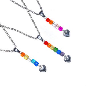 May include: Three silver necklaces with a rainbow-colored bead design. Each necklace has a chain, a pendant with a series of colorful beads, and a heart-shaped charm at the end. The beads are arranged in a rainbow spectrum.
