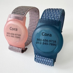 May include: Two wristbands with clear plastic ID tags. The tags are pink and blue and have the text "Cora" and phone numbers printed on them.