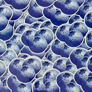 May include: A collection of blue blueberry stickers with cute faces. The stickers are arranged in a random pattern and are all different sizes.