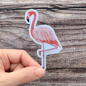 May include: Pink flamingo sticker with the word "FABULOUS" printed on the bottom. The sticker is on a wooden background.