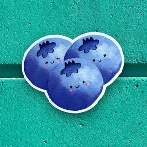 May include: Three blue blueberries with white outlines and happy faces. The blueberries are clustered together and have a watercolour-like appearance.