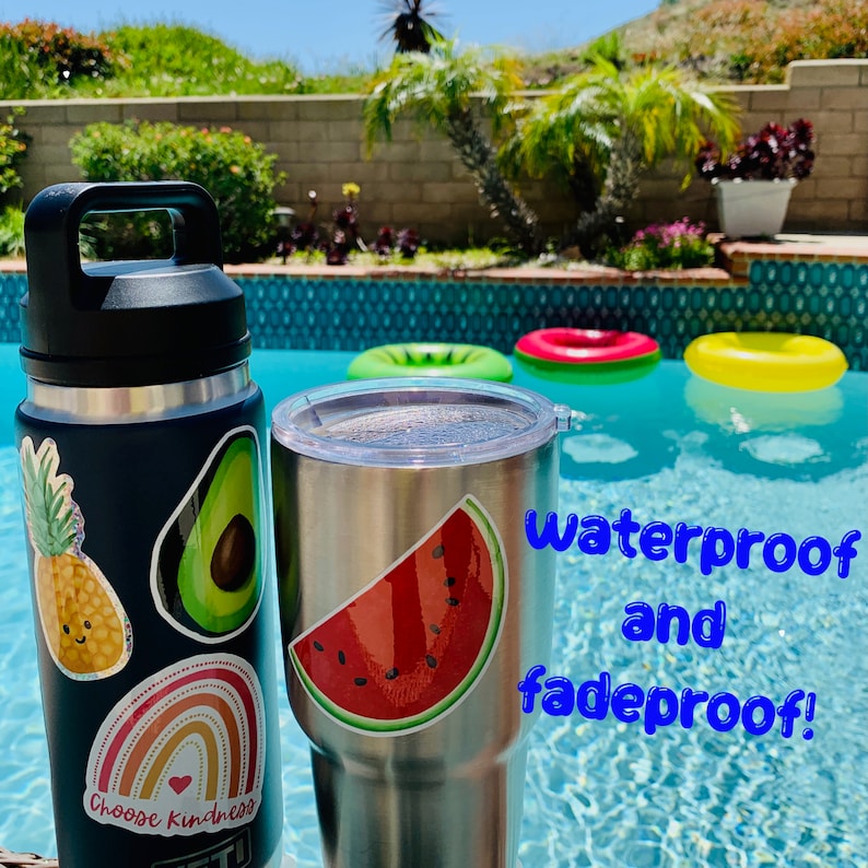 May include: Two stainless steel tumblers with colourful stickers. The tumbler on the left has a pineapple, avocado, and rainbow sticker. The tumbler on the right has a watermelon sticker. The text "Waterproof and fadeproof!" is written in blue on a background of a swimming pool.