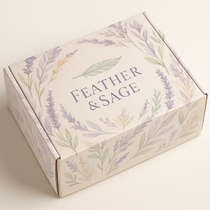 Puede incluir: Una caja de cartón blanca con un diseño floral con lavanda y salvia. La caja tiene el texto "FEATHER & SAGE" impreso en ella.
