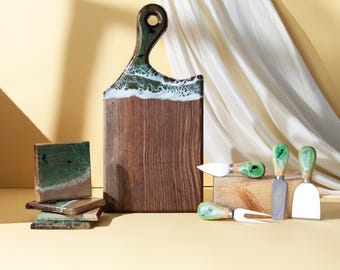 May include: A wooden serving board with a handle, featuring a green and white resin wave design. Includes a set of matching coasters and cheese knives with green handles. The wood has a natural grain.