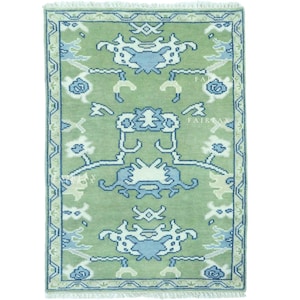 May include: Rectangular rug with a light green field and a detailed pattern in blue and off-white. The design features floral and geometric elements, with a border in a darker blue. The rug has a fringe on the short ends.