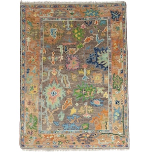 May include: A rectangular, hand-woven rug with a central field of brown and a border of orange. The rug features a complex pattern of colorful, stylized floral and geometric motifs in shades of blue, green, pink, and yellow. The rug is likely made of wool.