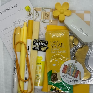 May include: A yellow and white stationery set with a reading log notebook, pens, highlighters, a lip balm, a face mask, a book-themed keyring, and a flower-shaped paperweight.