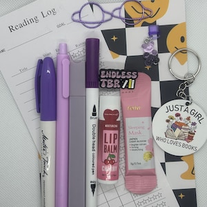 Op de afbeelding: Een leeslogboek, paarse pennen, een paarse marker, een lippenbalsem, een slaapmasker, een sleutelhanger met een boekthema-hanger en een kaart met de tekst "ENDLESS TBR" erop.