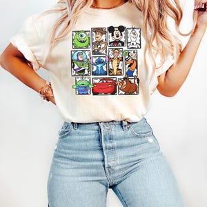 May include: Cream-colored t-shirt featuring a grid of cartoon characters including Mike Wazowski, Woody, Mickey Mouse, Olaf, Buzz Lightyear, Stitch, Tigger, and others. The shirt is paired with light blue denim jeans.
