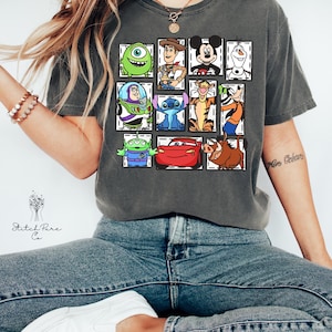 May include: Dark gray t-shirt featuring a grid of cartoon characters including Mike Wazowski, Woody, Mickey Mouse, Olaf, Buzz Lightyear, Stitch, Tigger, and Goofy. Other characters include the Alien, Lightning McQueen, and Pumbaa. The shirt has the text "Stitch Pure Co."