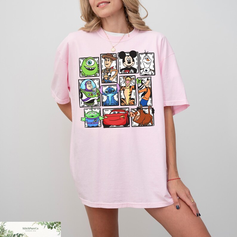 May include: A light pink t-shirt featuring a grid of cartoon character portraits. The characters include Mike Wazowski, Woody, Mickey Mouse, Olaf, Buzz Lightyear, Stitch, Tigger, Goofy, the Aliens, Lightning McQueen, and Pumbaa.