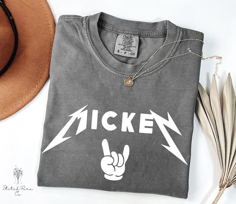 May include: A gray Comfort Colors t-shirt with the word "MICKEY" in a white, stylized font, and a white hand gesture. A silver necklace with a pendant is on the shirt.