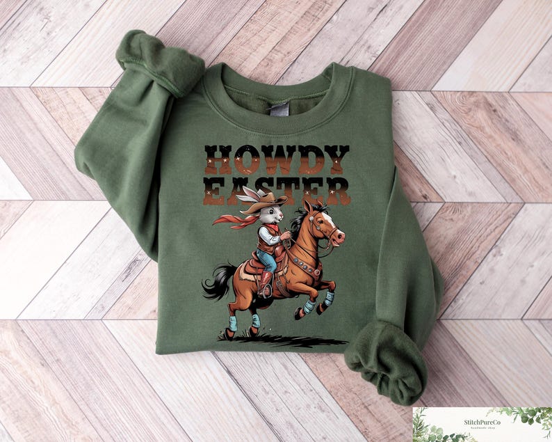 May include: Green crewneck sweatshirt with the text "HOWDY EASTER" above an illustration of a cowboy rabbit riding a horse. The rabbit wears a cowboy hat and red scarf. The horse is brown and the sweatshirt has rolled sleeves.