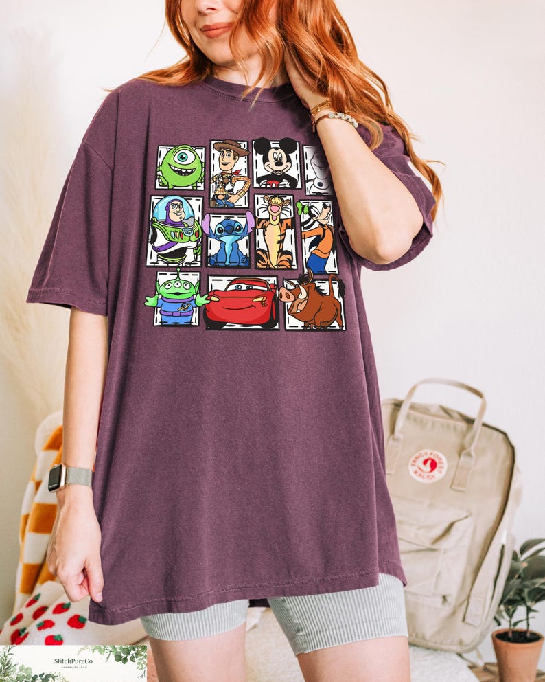 May include: A maroon oversized t-shirt featuring a grid of cartoon characters including Mike Wazowski, Woody, Mickey Mouse, Buzz Lightyear, Stitch, Tigger, and others. The shirt has a relaxed fit and short sleeves.