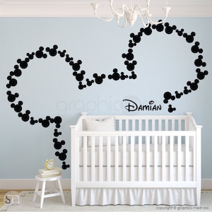 May include: Black Mickey Mouse head wall decal with the name "Damian" in a nursery setting. The decal is made of small, connected circles. A white crib, small table, and clock are in the foreground.