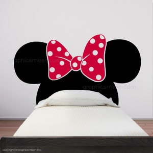 Pode incluir: Silhueta preta e branca da cabeça da Minnie Mouse com um laço vermelho com bolinhas brancas. A silhueta está em uma parede branca acima de uma cama branca com uma cabeceira preta.