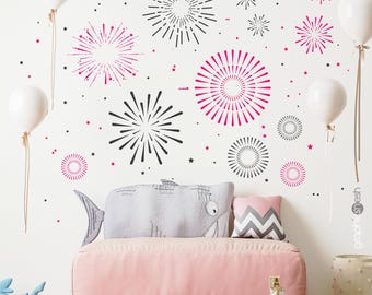 May include: A wall decal set featuring black and pink firework bursts and small stars. The design includes various circular patterns of radiating lines in different sizes, arranged to create a festive display on a plain white wall surface.