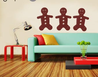 May include: Three brown gingerbread man wall decals featuring white icing details, including a smiling face and three circular buttons on the torso. The decals are arranged horizontally on a plain wall above a light blue sofa with cushions.