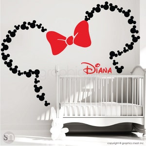 May include: A white wall with a black and red Mickey Mouse themed wall decal. The decal features a red bow and the name "Diana" in red lettering. A white crib is in the background.