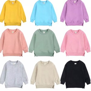 May include: Nine plain crew neck sweatshirts in various colors, including yellow, light blue, purple, pink, green, light pink, gray, beige, and black.