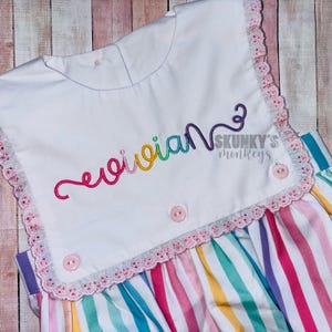 May include: A white baby dress with a rainbow striped skirt and a white bodice with a rainbow embroidered name "evie" and the text "Skunky's monkeys".