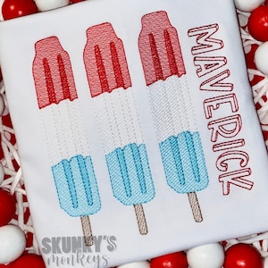 May include: White t-shirt with three red, white, and blue popsicle designs and the word "Maverick" in red outlined letters.