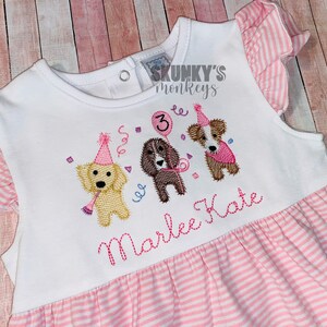 May include: White and pink striped dress with embroidered puppies wearing party hats and holding a balloon with the number 3. The dress has pink striped sleeves and the name "Marlee Kate" embroidered on the front.