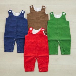 May include: Four pairs of corduroy overalls in different colors: navy blue, brown, green, and red. The overalls have a simple design with two pockets and a button closure.