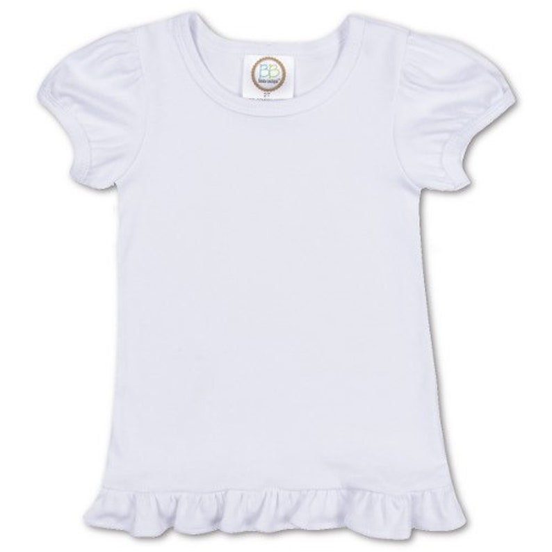 May include: White short-sleeved t-shirt with a ruffled hem. The shirt has a small tag with the text "BB Designs" on the front.