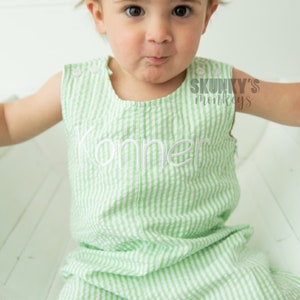 May include: A green and white striped romper with the name "Konner" embroidered on the front. The romper has a sleeveless design and is made of a soft, comfortable fabric.