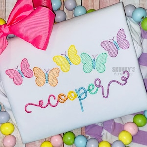 May include: A white onesie with a rainbow embroidered name "cooper" and a row of colorful butterflies.