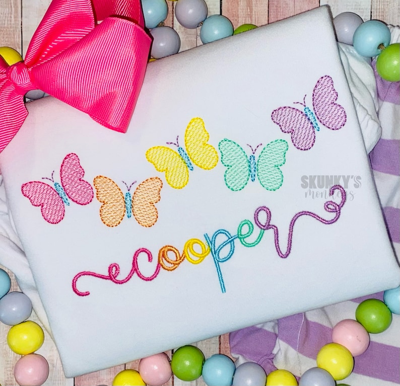 May include: A white onesie with a rainbow embroidered name "cooper" and a row of colorful butterflies.