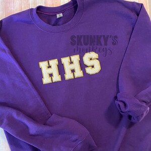 May include: Purple sweatshirt with the text "SKUNKY'S monkeys" and "HHS" in gold glitter letters.