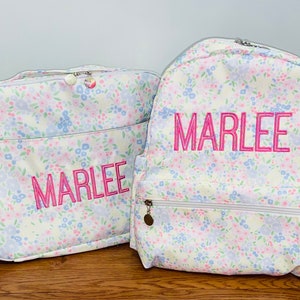 May include: A white floral backpack and matching lunch bag with the name "Marlee" embroidered in pink.
