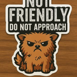 May include: A sticker with the text "NOT FRIENDLY DO NOT APPROACH" above a cartoon illustration of a grumpy, brown, fluffy dog. The dog has a stern expression with furrowed brows and a downturned mouth.