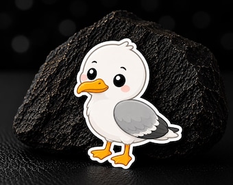 May include: A sticker featuring a cartoon seagull with a white head, grey wings, and orange feet and beak. The bird has large black eyes and pink cheeks. The sticker is placed against a dark, textured, rock-like background with a subtle bokeh effect.